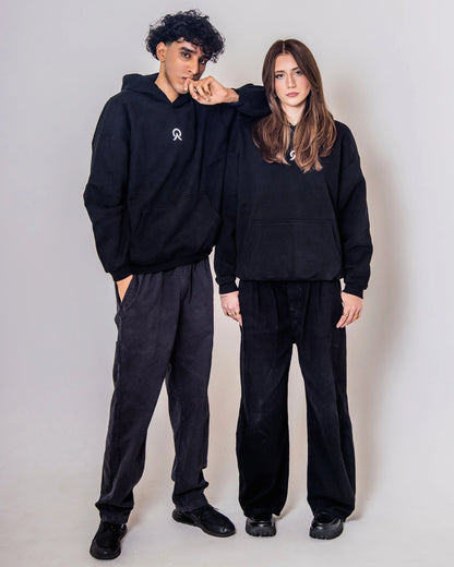 Two people wearing matching black hoodie and pants outfits against a plain background