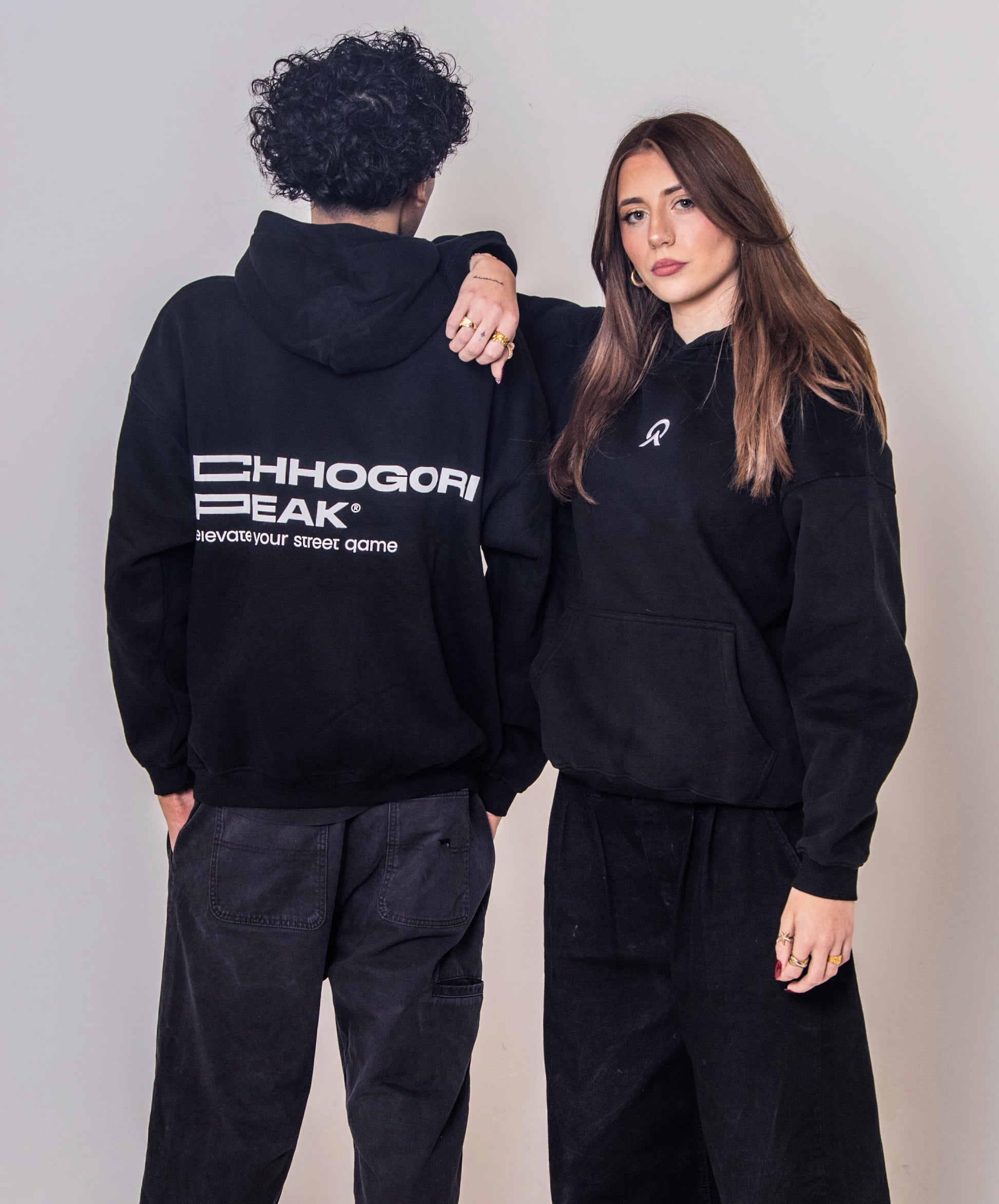 Two people wearing matching black hoodie and pants outfits against a plain background